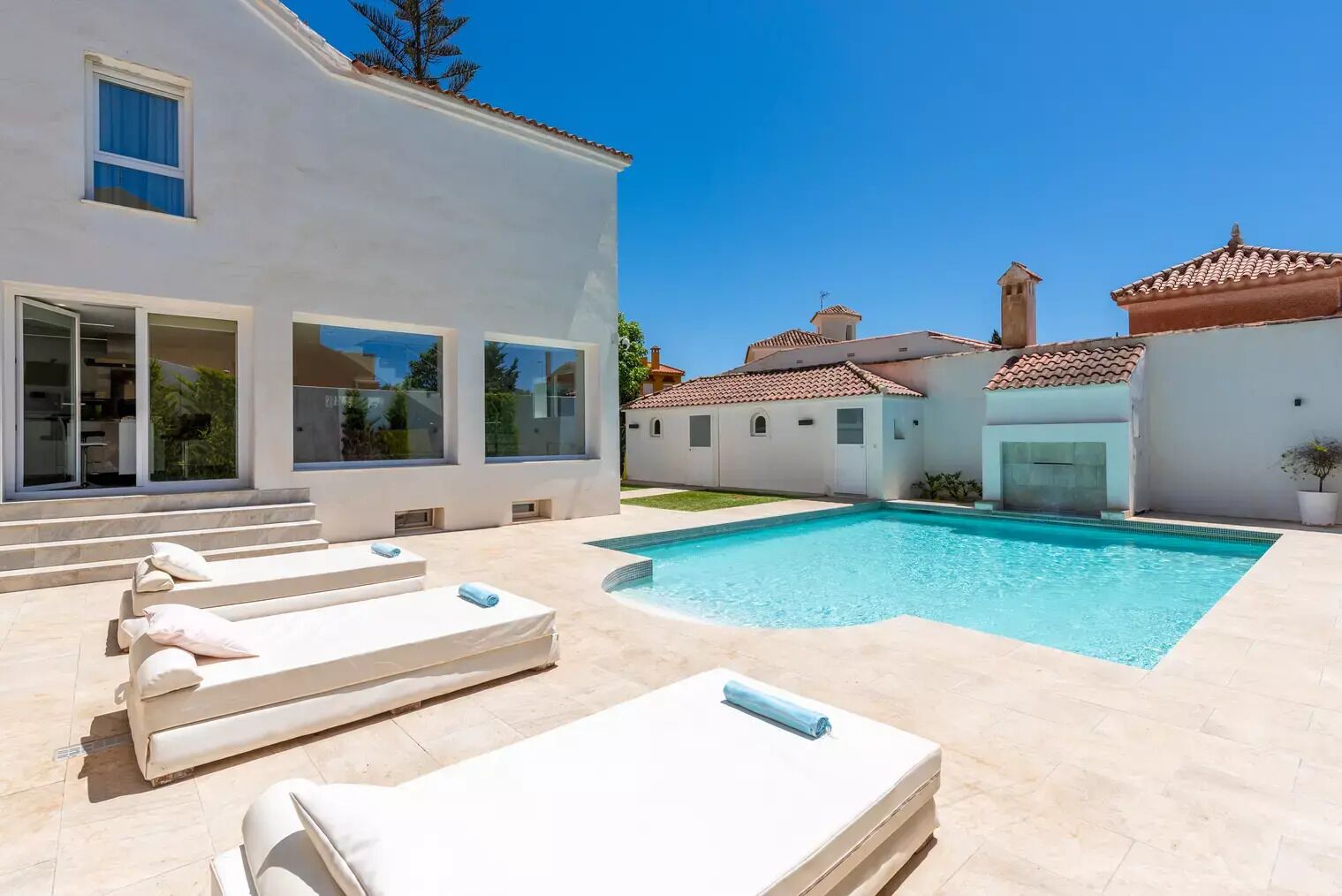 A modern house with a swimming pool, outdoor seating, and a clear blue sky.