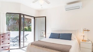 Ein Schlafzimmer mit Bett, Nachttisch, Lampe, Kommode und einer Glasschiebetür zu einem Außenbereich mit Stuhl und Tisch.