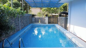 Una piscina rectangular con borde de azulejos, una escalera de metal y un área cubierta con techo azul.