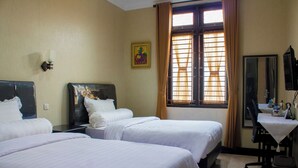 Habitación de hotel con tres camas, un escritorio con silla, televisión y ventana con cortinas.