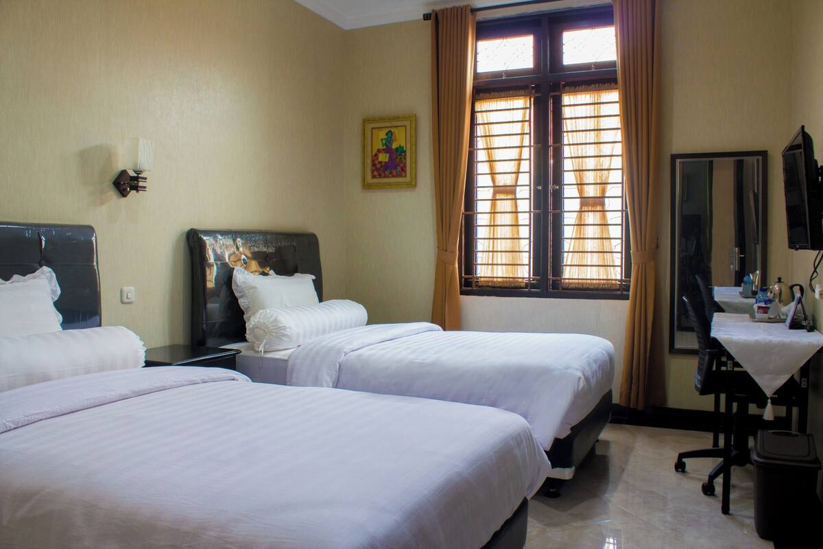 Habitación de hotel con tres camas, un escritorio con silla, televisión y ventana con cortinas.