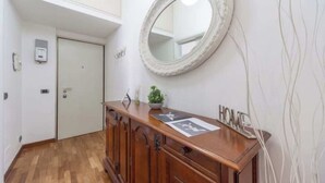 A hallway with a wooden cabinet, a round mirror, and a door. - House Romana Center (Milano)
