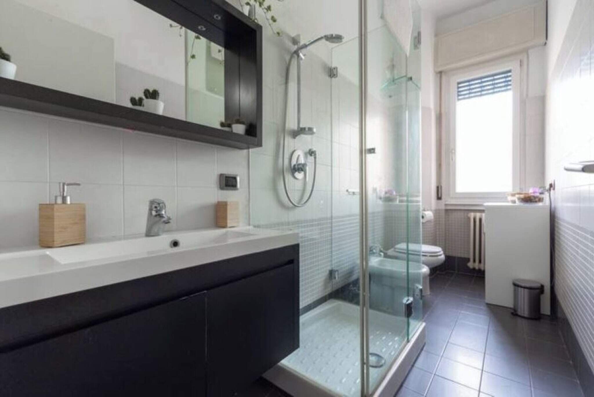 Ein modernes Badezimmer mit einer Duschkabine aus Glas, einem großen Spiegel und einem weißen Waschbecken.