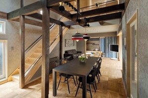 A spacious dining area with a long table and chairs, a staircase with a wooden railing, and a hanging pendant light. - Waren Bettei Machiya House (Kyoto)