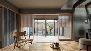 A modern interior with a wooden bench, a small table with a teapot, and sliding doors leading to a garden. - Waren Bettei Machiya House (Kyoto)