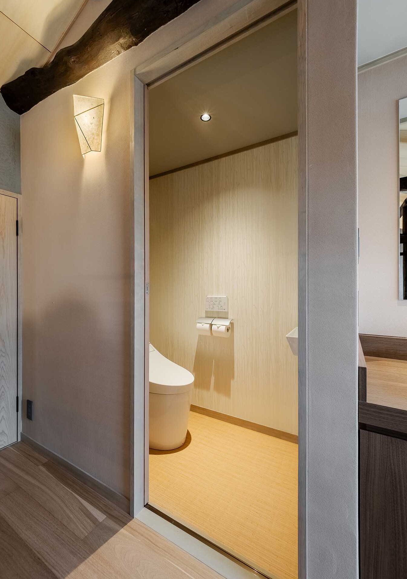 A modern bathroom with a toilet, a wooden floor, and a light fixture on the wall.