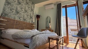A bedroom with a bed, a wooden bench, a fluffy rug, a mirror, and a balcony with a view. - Tropical style suite (Licata)