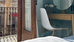 A bedroom with a bed, a wooden desk, a white chair, a round mirror, and a view of the outside balcony. - Tropical style suite (Licata)