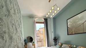 A bedroom with two beds, a desk, and a chair. There is a window with a view of buildings outside. - Tropical style suite (Licata)