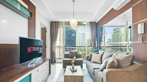 Una sala de estar moderna con un televisor de pantalla plana grande, un sofá, una mesa de centro y vistas de la ciudad a través de amplios ventanales.