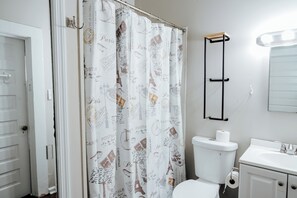 Une salle de bain avec un rideau de douche orné de motifs parisiens, des toilettes, un lavabo et un miroir.