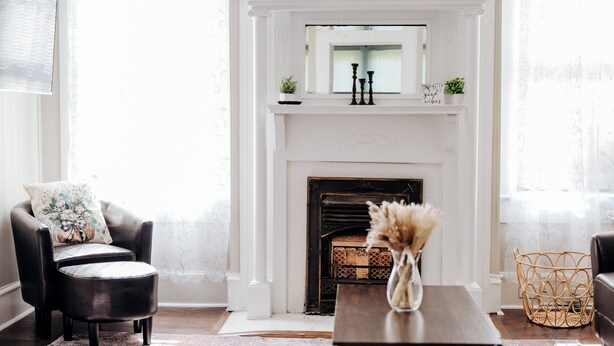 A living room with a white fireplace, a black leather armchair, a wooden coffee table, and a wicker basket. - Minutes from Maxwell AFB, this historic 3BR feels more like home than a rental. Guests love the quiet street, thoughtful touches, and a host who makes every stay easy. (Montgomery)