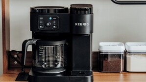 A coffee maker on a wooden shelf with a coffee pod holder and a coffee grinder below. - Minutes from Maxwell AFB, this historic 3BR feels more like home than a rental. Guests love the quiet street, thoughtful touches, and a host who makes every stay easy. (Montgomery)
