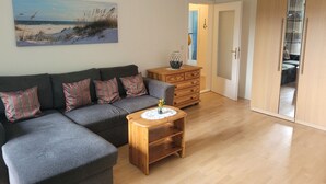 A living room with a grey sofa, a wooden coffee table, and a painting of a beach scene. - Family accommodation Moin Moin (Schilksee)