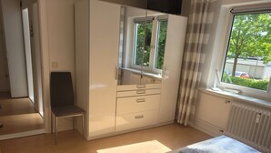 A bedroom with a bed, a wardrobe, a chair, and a window with a view of greenery and parked cars. - Family accommodation Moin Moin (Schilksee)