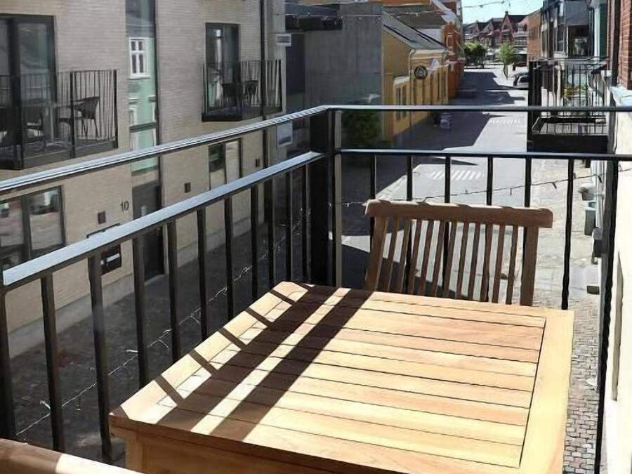 A balcony with a wooden table and chairs, overlooking a street with buildings and a church spire.