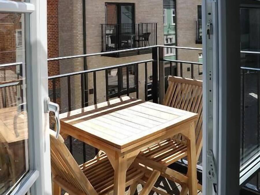 A balcony with a wooden table and chairs, a glass door, and a building with brick walls and balconies in the background.