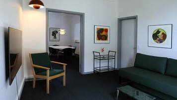 A modern living room with a green sofa, a wooden chair, a glass coffee table, and artwork on the walls.