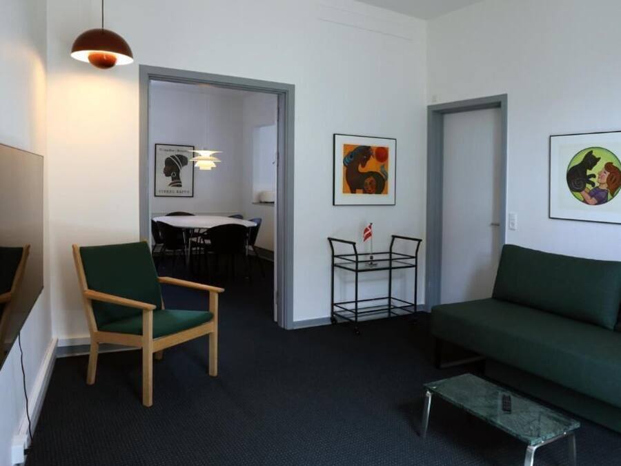 A modern living room with a green sofa, a wooden chair, a glass coffee table, and artwork on the walls.
