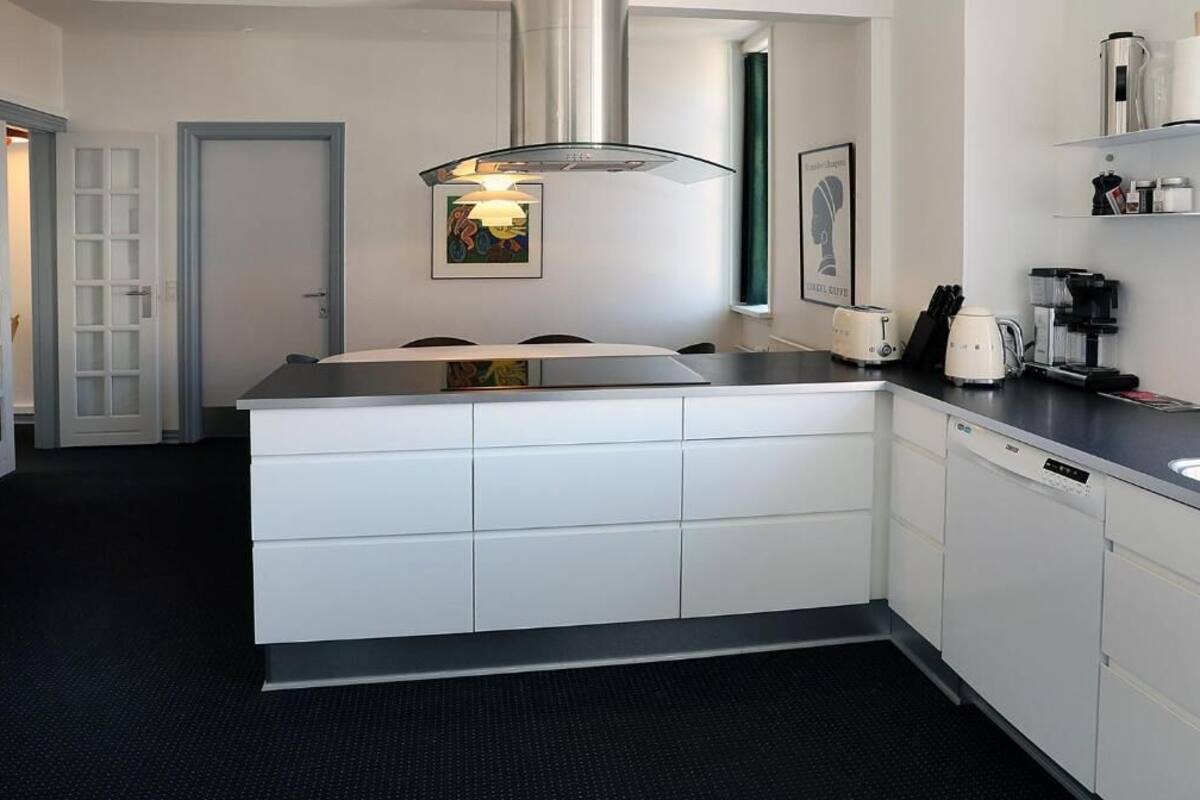 A modern kitchen with white cabinetry, a black countertop, and a stainless steel range hood. There are two coffee makers and a toaster on the counter.