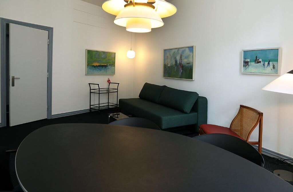 A conference room with a large table, a green sofa, and three paintings on the walls.
