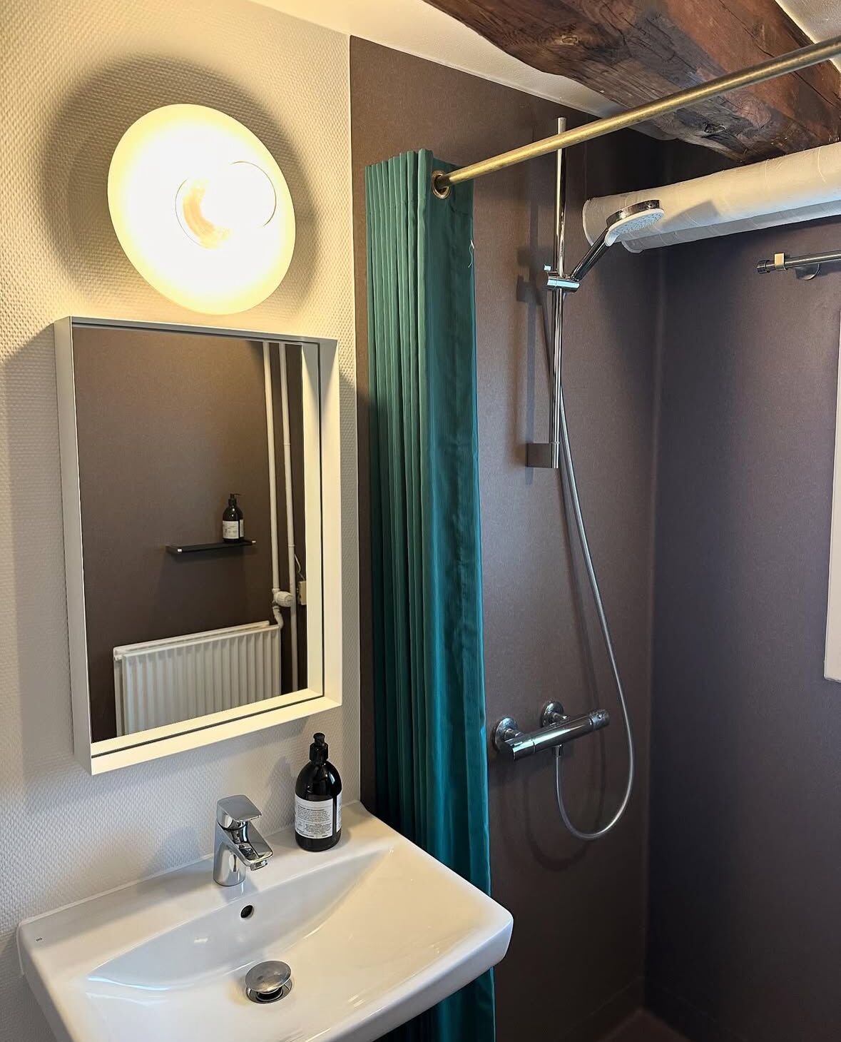 Un baño con lavamanos, espejo, ducha y perchero.
