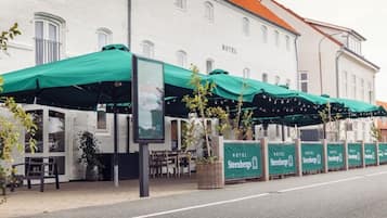 A hotel with outdoor seating under green awnings, a signboard, and a row of identical signs along the sidewalk.