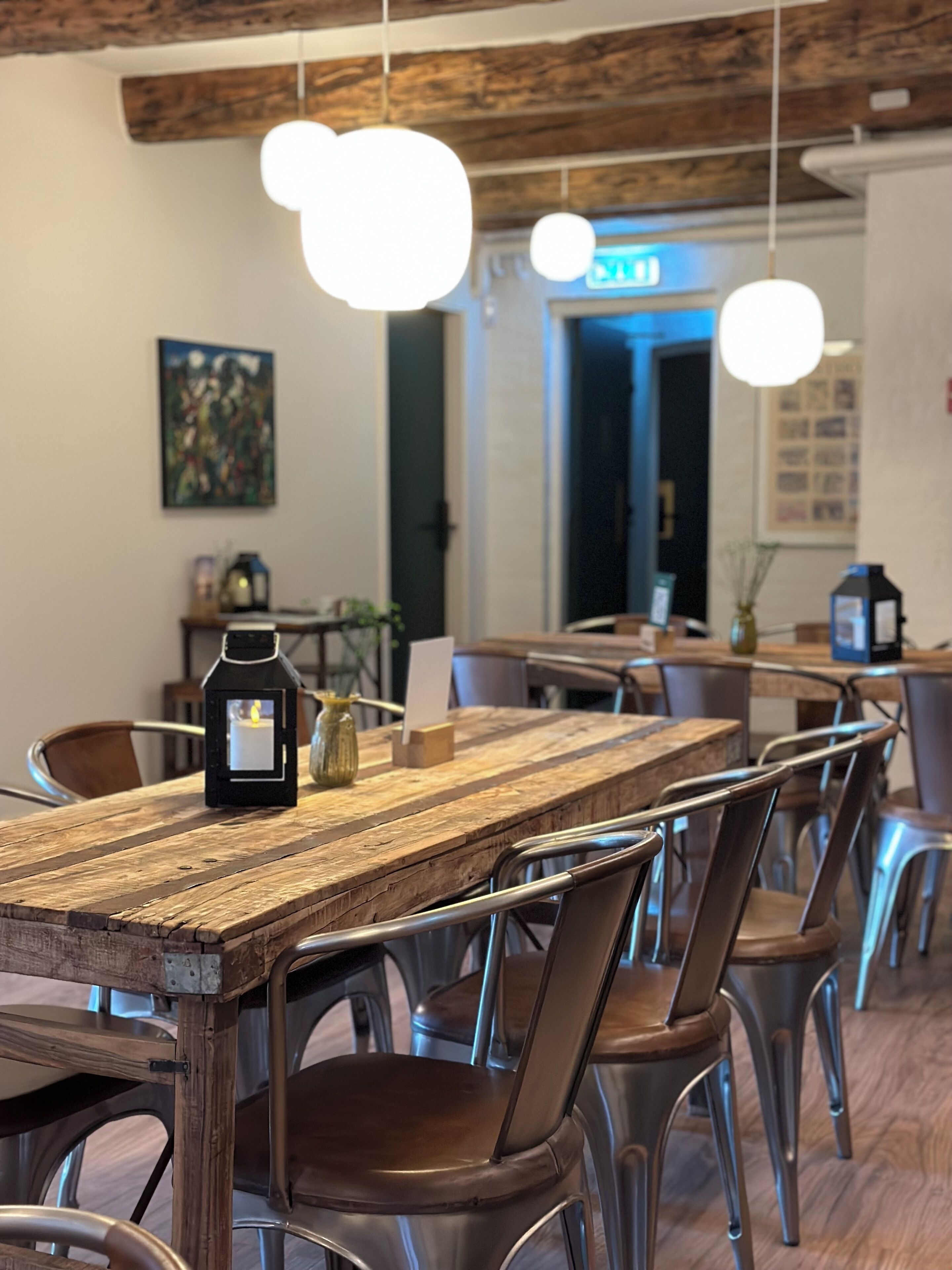 Un espace repas avec une table en bois rustique, des chaises en métal et des luminaires suspendus.