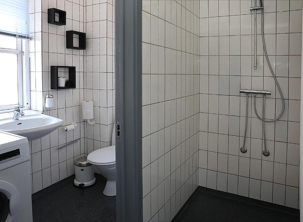 Uma casa de banho moderna com azulejos brancos, sanita, lavatório e chuveiro.