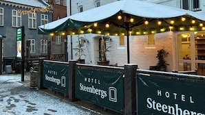 Hotelli nimeltä »Steenbergs», jossa on kyltti, katettu ulkoalue, jossa on valoketjuja, ja lumipeitteinen maa.