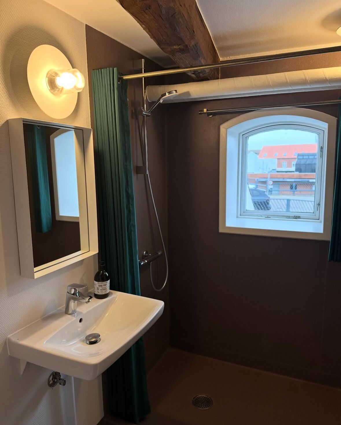 A bathroom with a sink, mirror, shower, and a window with a view of buildings.
