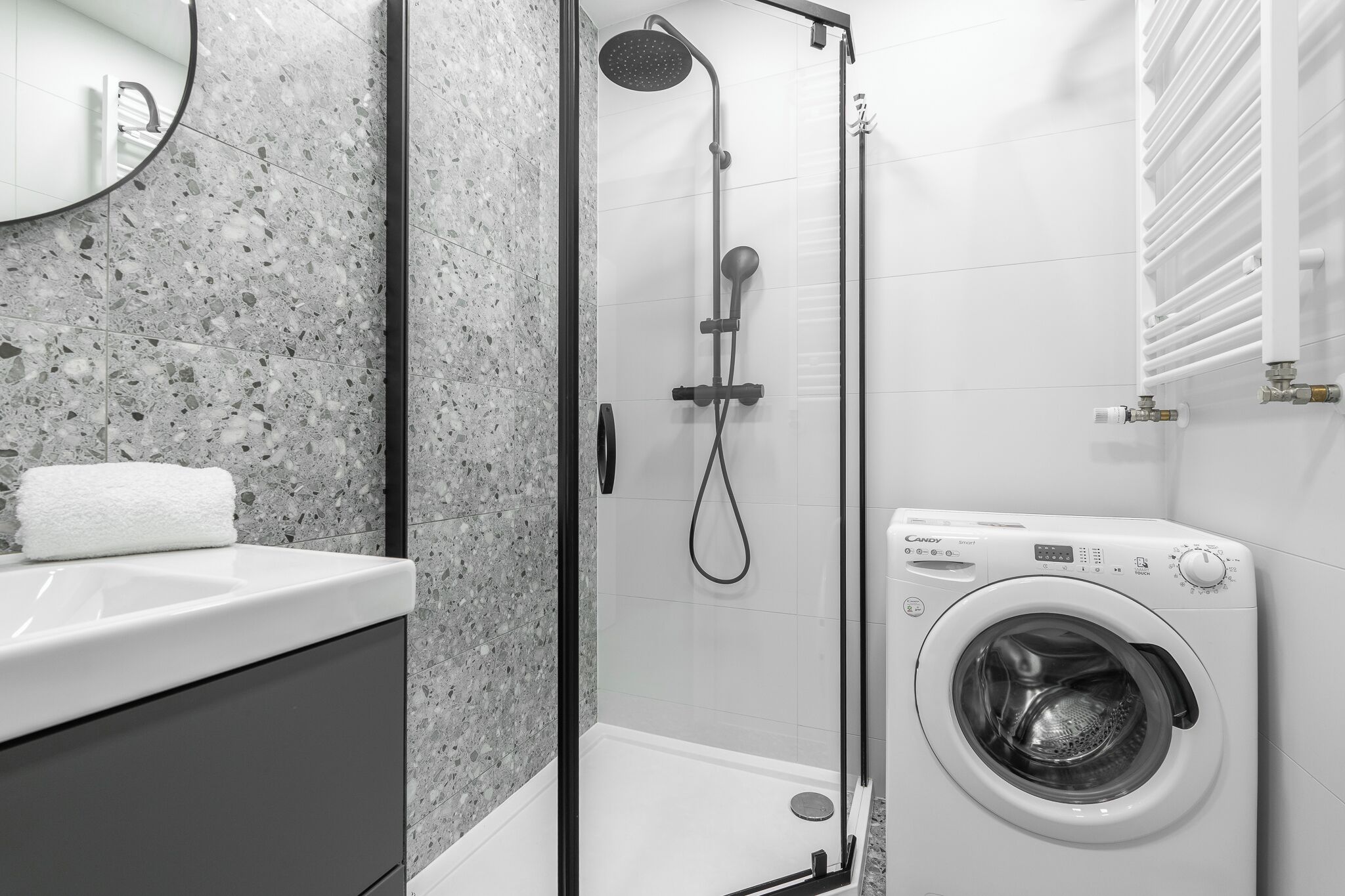A modern bathroom with a granite countertop, a glass-enclosed shower, and a front-loading washing machine.
