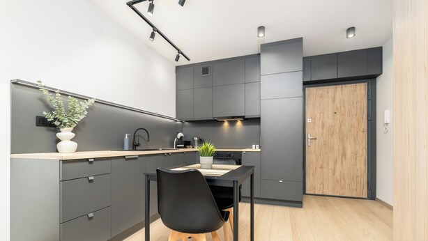 A modern kitchen with grey cabinets, a wooden door, and a dining table with chairs.