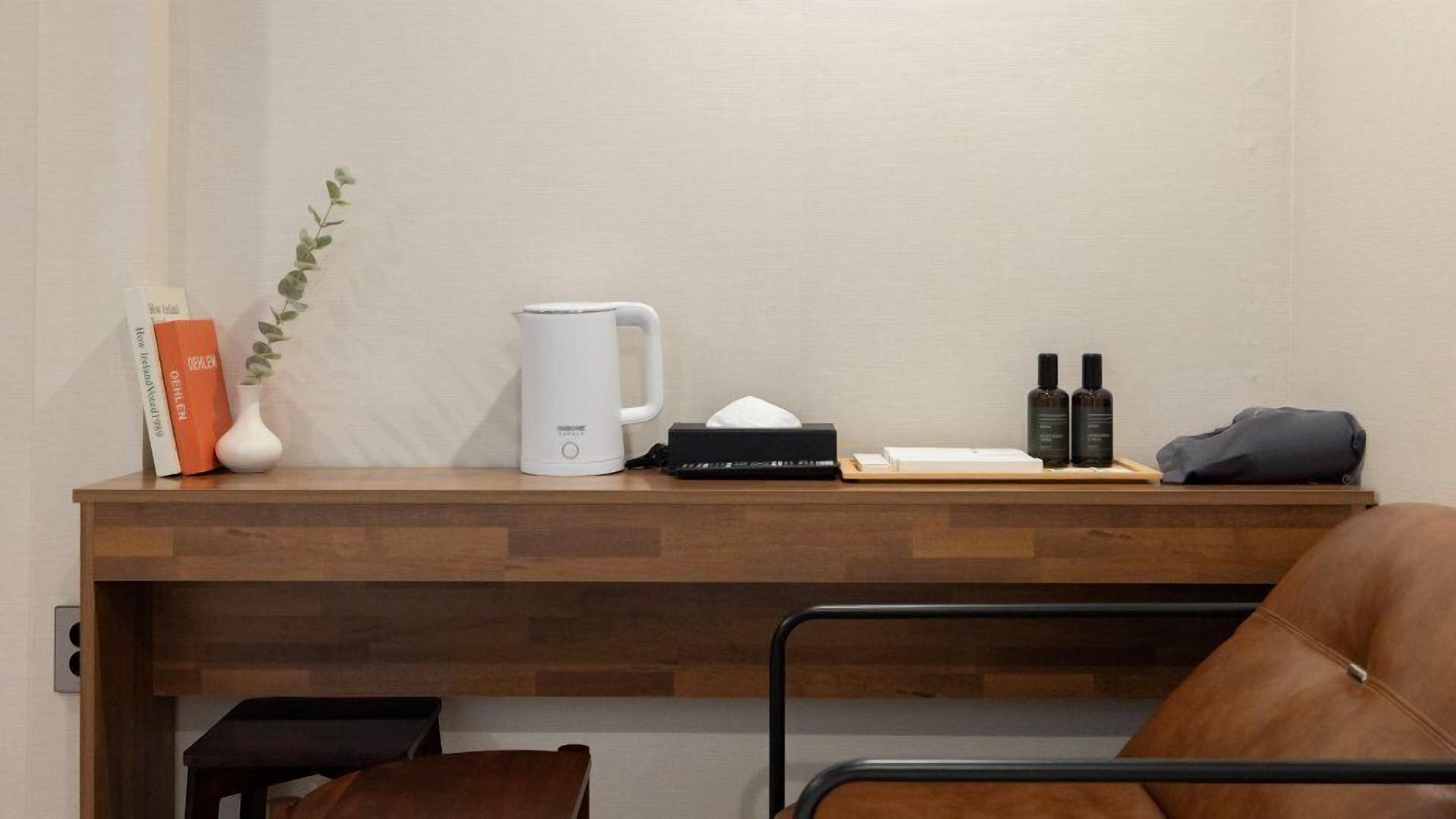 Een houten bureau met een witte koffiezetapparaat, een zakdoos, twee flessen en een boek.