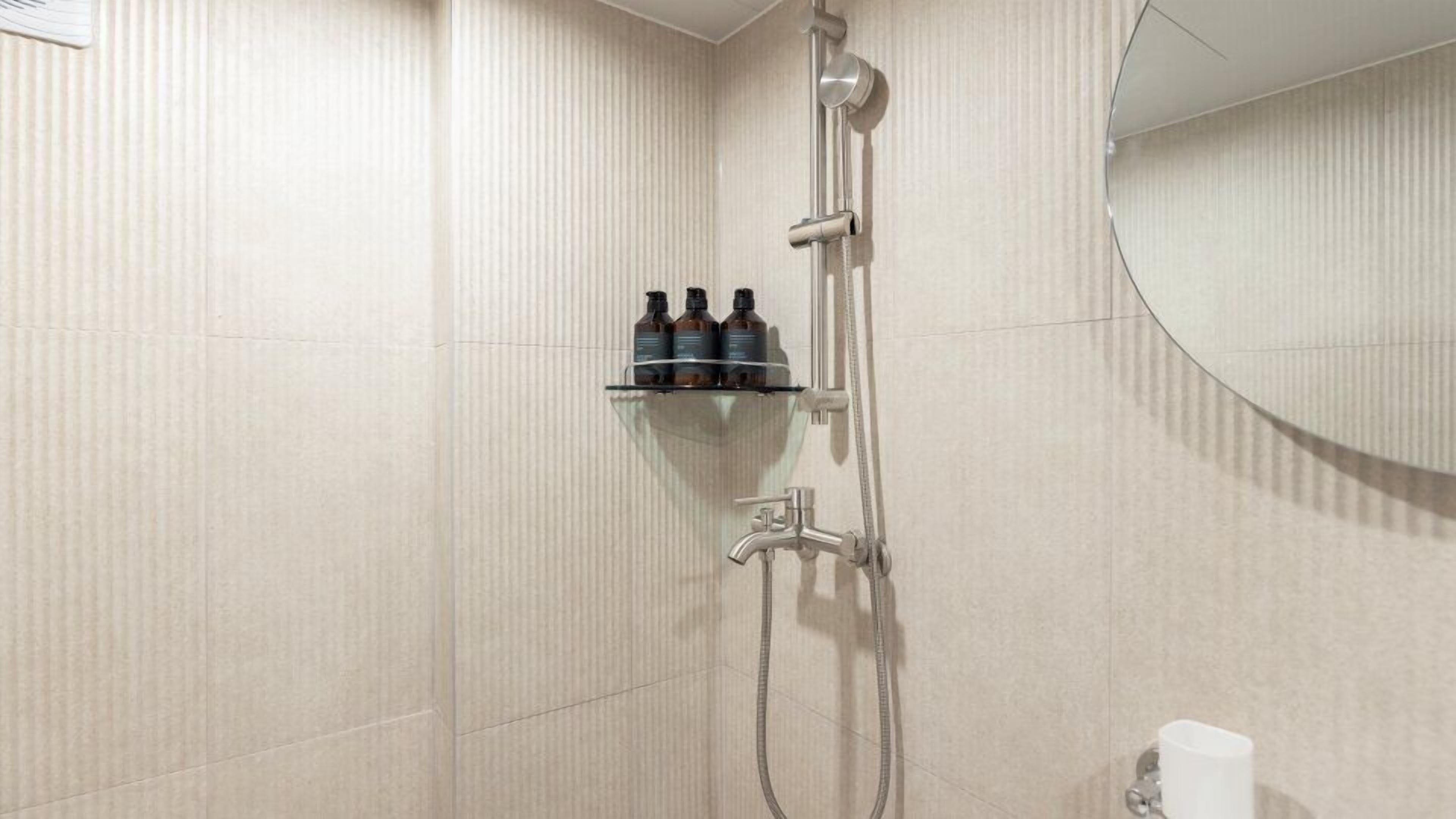 Eine Dusche mit Ablage für Toilettenartikel, einer Handbrause und einem am Wand montierten Wasserhahn.