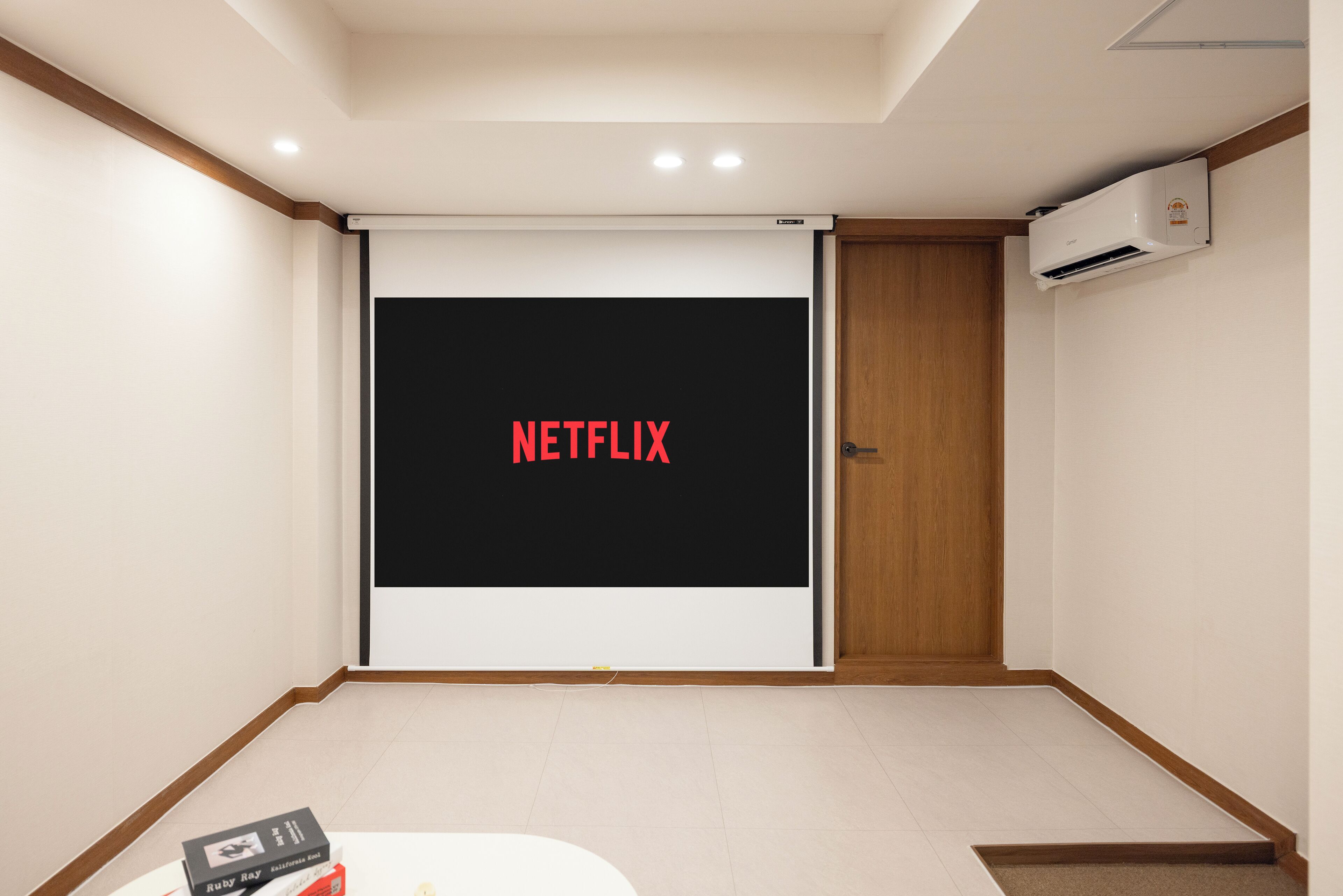 A room with a large screen displaying 'NETFLIX' in red letters, a door, and an air conditioning unit on the wall.