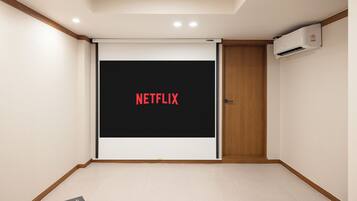 Ein Zimmer mit einem großen Bildschirm, der 'NETFLIX' in roten Buchstaben zeigt, einer Tür und einer Klimaanlage an der Wand.