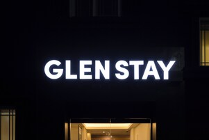 Un letrero de hotel con el nombre 'GLEN STAY' iluminado en letras blancas sobre un fondo oscuro.