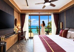 Ein Hotelzimmer mit einem großen Bett, einem Schreibtisch mit Stuhl, einem Fernseher und einem Balkon mit Meerblick.