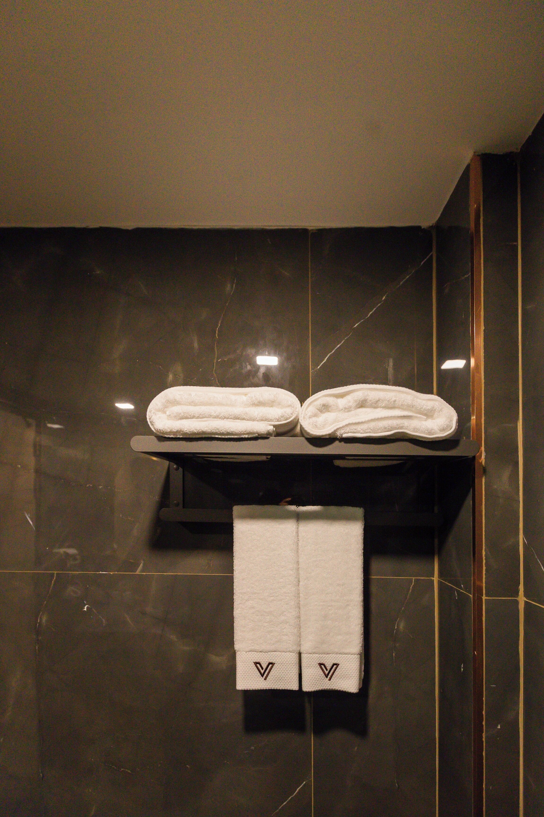 A bathroom with dark marble walls, a towel rack with two folded towels, and a single towel hanging below.