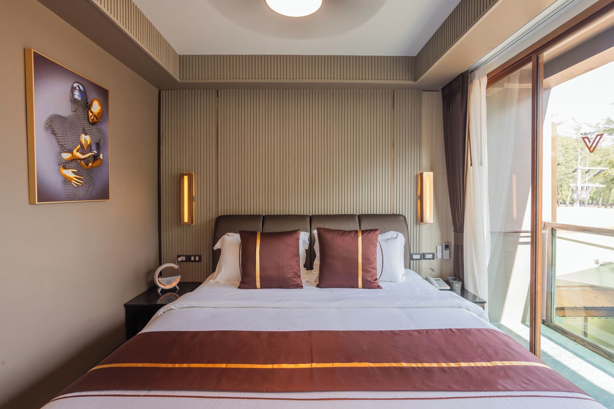 A hotel room with a large bed, two bedside tables, a wall-mounted artwork, and a view through a large window.