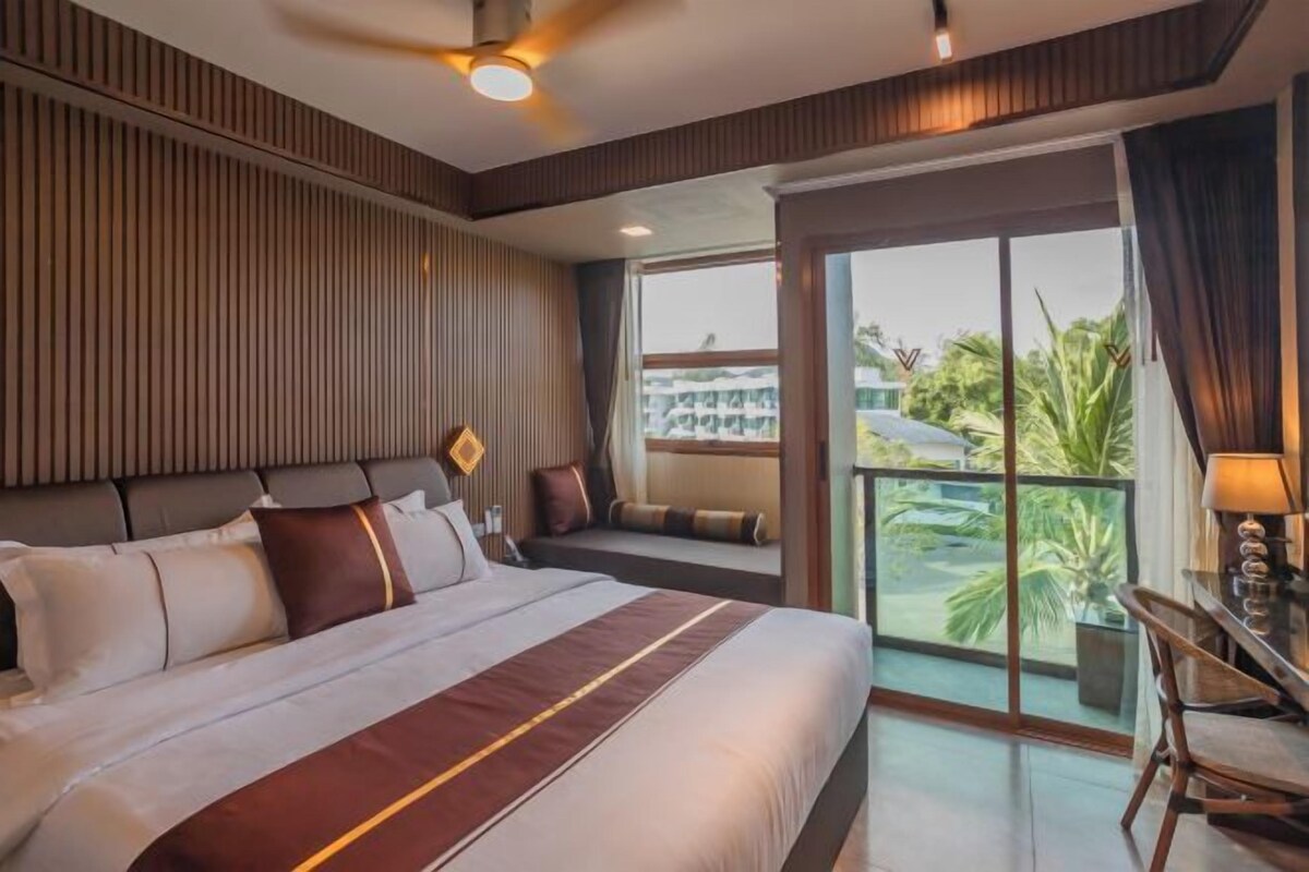 A hotel room with a large bed, a balcony with a view, and a desk with a lamp.