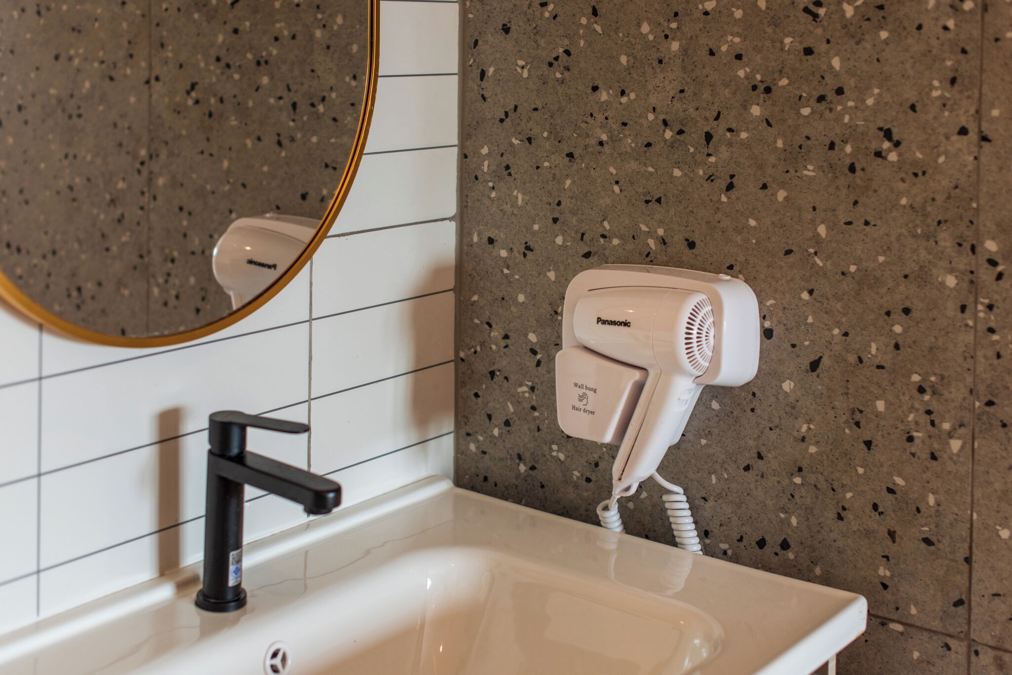 A bathroom with a white sink, black faucet, and a Panasonic hair dryer on a wall-mounted charging station.