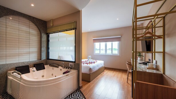 A modern bathroom with a large bathtub, a shower, and a vanity. There is a bed with a white canopy and a window with a view of the outdoors. - THE MOMENT (Khlong Luang)