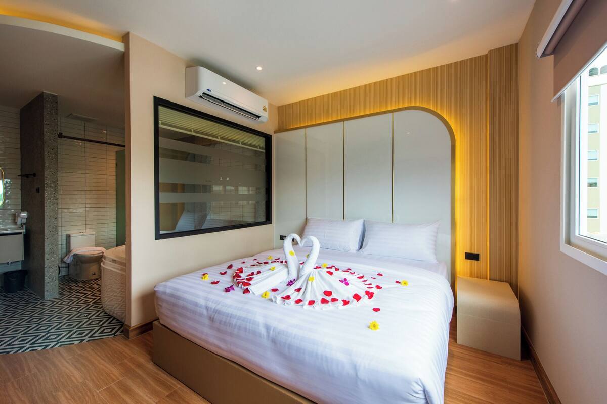 Habitación de hotel con una cama grande, aire acondicionado integrado, zona de ducha y vistas a la ciudad desde la ventana.