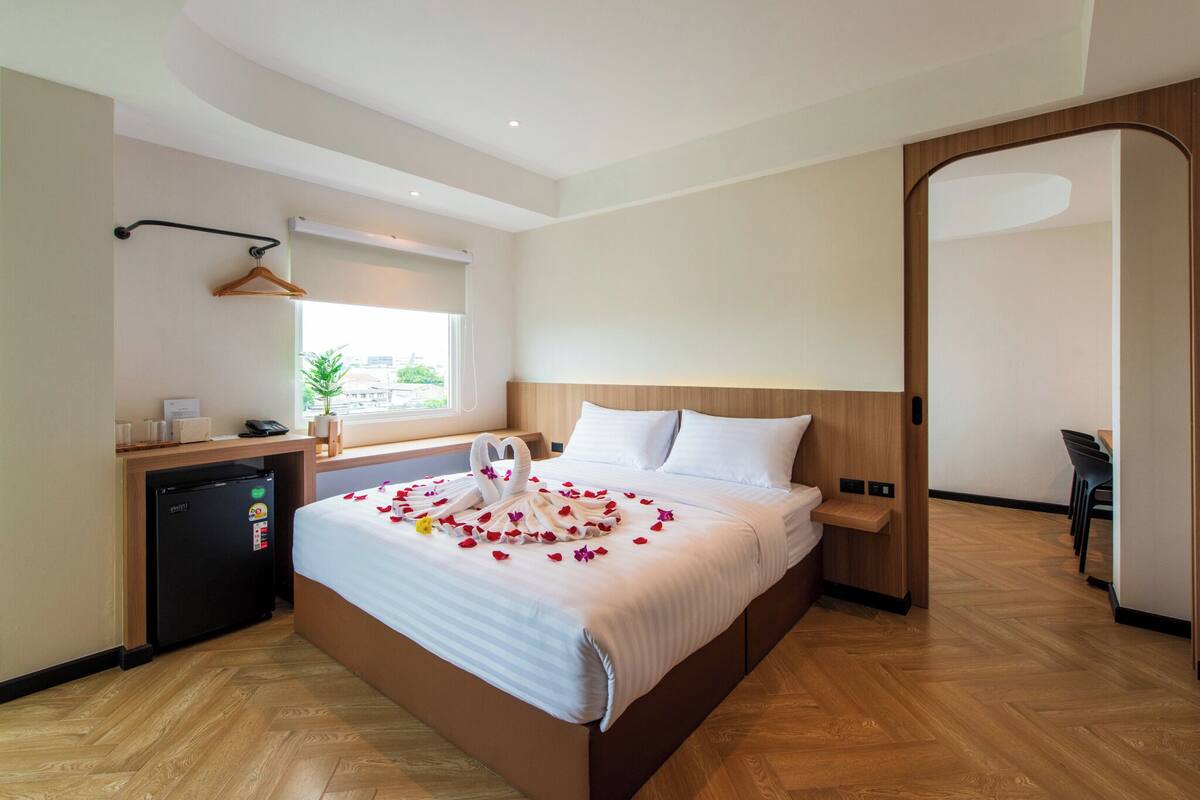 Habitación de hotel con cama, escritorio, refrigerador, ventana con vistas y suelo de madera.