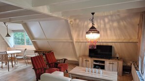 A cozy living area with a TV, red and white chairs, a small table, and a hanging chandelier.