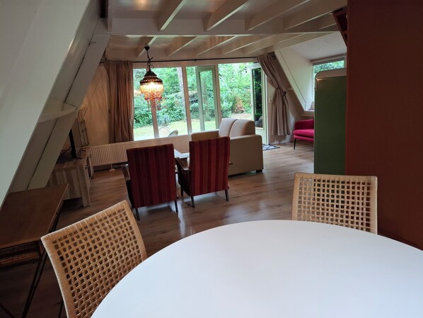 An attic room with a dining table and chairs, a sofa, and a hanging light fixture.