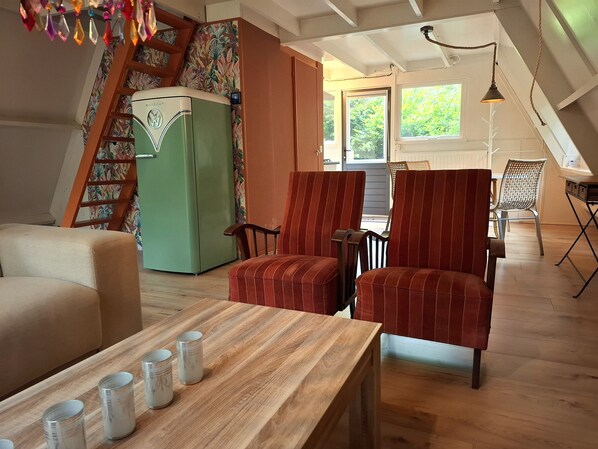 A cozy living room with a wooden table, striped chairs, a green refrigerator, and a staircase with a floral wallpaper.