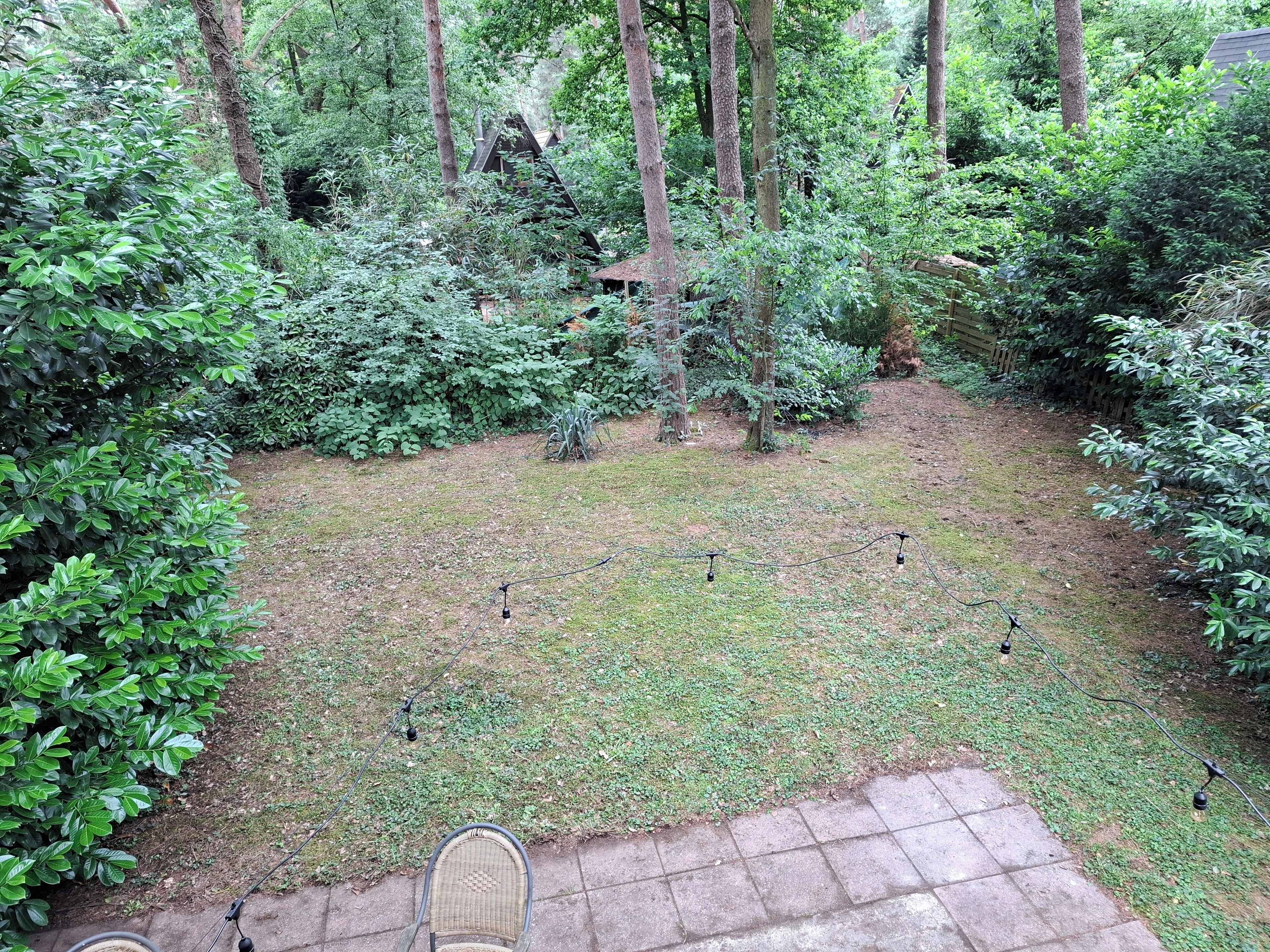 Un giardino con un patio lastricato e una sedia in vimini.